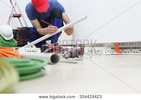 Electrician At Work With Pencil In Hand Measures The Plastic Pipe To Pass The Electric Cables To The