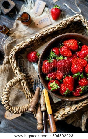 Overhead Shot Of Tasty Ripe Strawberries In Wooden Bowl Stands In Wicker Strawy Basket On Rustic Tab