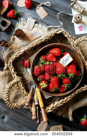 Overhead Shot Of Tasty Ripe Strawberries In Wooden Bowl Stands In Wicker Strawy Basket On Rustic Tab