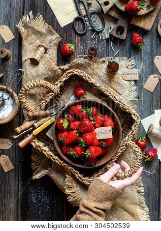 Overhead Shot Of Tasty Ripe Strawberries In Wooden Bowl Stands In Wicker Strawy Basket On Rustic Tab