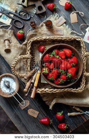 Overhead Shot Of Tasty Ripe Strawberries In Wooden Bowl Stands In Wicker Strawy Basket On Rustic Tab