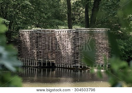 Wooden Building On The Shore Of The Pond. Wicker Building In The Forest.