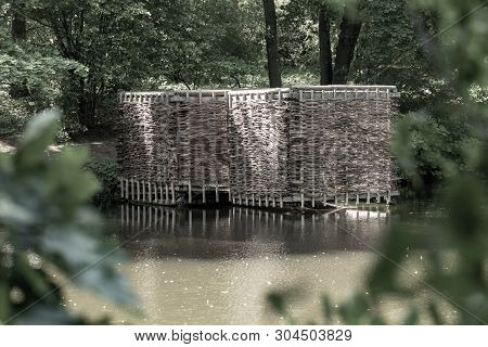 Wooden Building On The Shore Of The Pond. Wicker Building In The Forest.