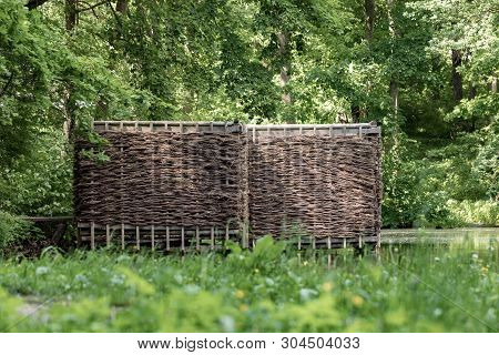 Wooden Building On The Shore Of The Pond. Wicker Building In The Forest.