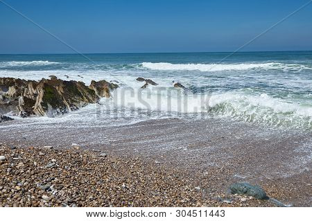 Pebble Beach And Sharp Stones On A Ocean Coast. The Wave Breaks On A Stone. Sea Water