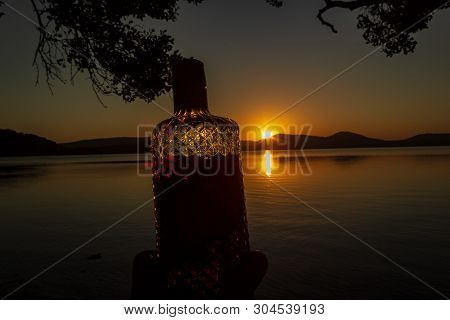 Beautiful Rum Bottle Full With Rum Holding In Front Of A Sunset Over Watson Taylors Lake At Crowdy B