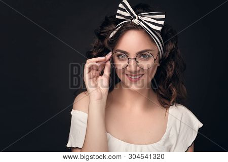 Close-up Portrait Of A Young Girl With Warm Beautiful Hair In Round Glasses And Bow On Head On A Dar