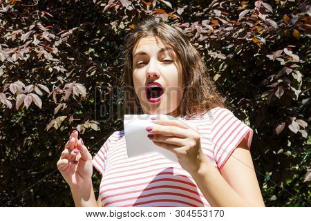 Allergy Concept. Sneezing Young Girl With Nose Wiper Among Blooming Trees In Park