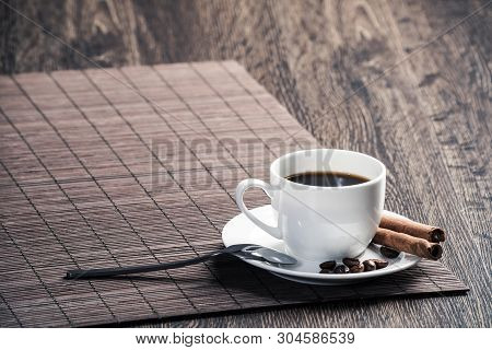 Cup Of Espresso Coffee On Wooden Table With Bamboo Mat. Coffee Beans And Cinnamon Sticks On White Po