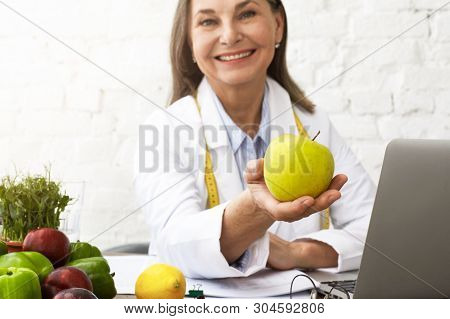 Indoor Image Of Attractive Professional Female Nutritionist In Her Sixties Smiling Broadly At Camera