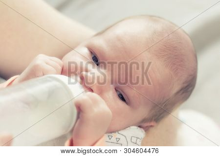 Portrait Of Cute Newborn Boy Drinking Milk From Bottle Looking At The Camera.