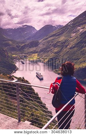 Female Tourist With Norwegian Flag Enjoying Scenic View Over Fjord Geirangerfjord With Cruise Ship. 