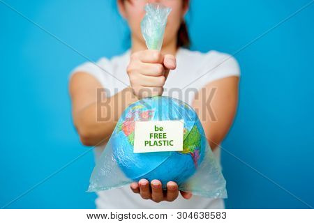 Woman holds in hands plastic bag with sticker text be FREE PLASTIC and planet earth at blue background. The concept of plastic pollution.