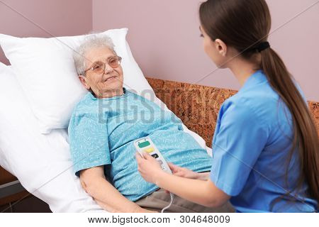 Nurse Assisting Senior Woman Lying On Bed In Hospital Ward