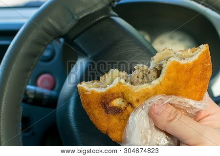 Pie, Belyash With Meat In The Hand Of The Driver In The Car On The Background Of The Steering Wheel 