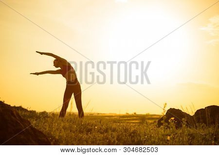 Young Woman Doing Stretching Outdoor. Warm up Exercise Against a Hot Beautiful Summer Sunset. Sport and Healthy Active Lifesyle Concept.