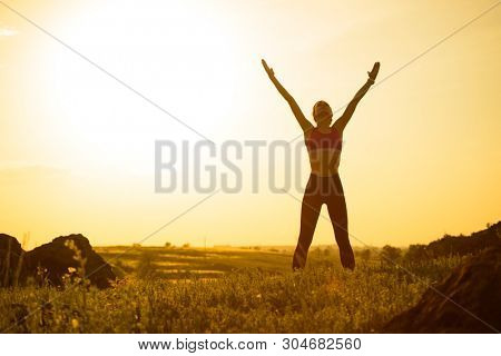 Young Woman Doing Stretching Outdoor. Warm up Exercise Against a Hot Beautiful Summer Sunset. Sport and Healthy Active Lifesyle Concept.