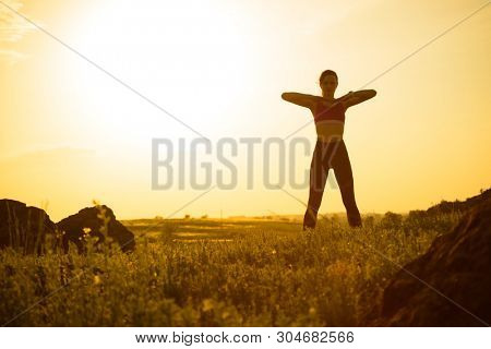 Young Woman Doing Stretching Outdoor. Warm up Exercise Against a Hot Beautiful Summer Sunset. Sport and Healthy Active Lifesyle Concept.