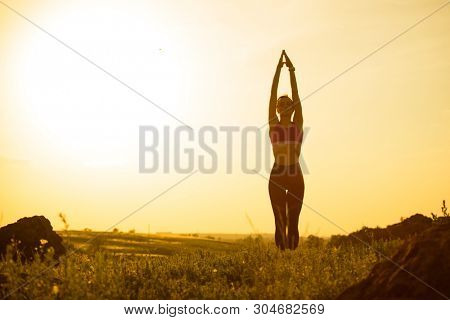 Young Woman Doing Stretching Outdoor. Warm up Exercise Against a Hot Beautiful Summer Sunset. Sport and Healthy Active Lifesyle Concept.