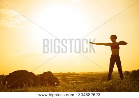 Young Woman Doing Stretching Outdoor. Warm up Exercise Against a Hot Beautiful Summer Sunset. Sport and Healthy Active Lifesyle Concept.