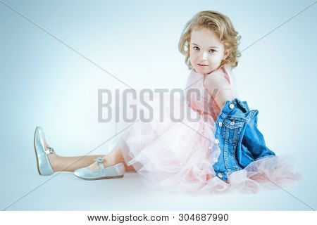 A full length portrait of a pretty girl in a pink dress and a denim jacket posing in the studio over the white background. Kids, fashion, beauty.