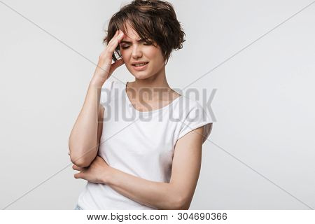 Photo of stressed woman with short brown hair in basic t-shirt grabbing her head and rubbing temples because of headache isolated over white background