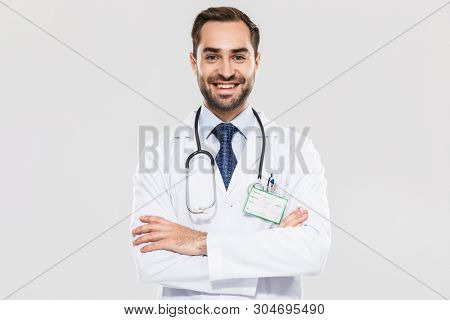 Portrait of brunette young medical doctor with stethoscope smiling at camera and standing wth arms crossed isolated over white background