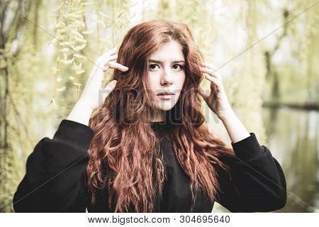 Beautiful Redhead Young Woman Under The Willow Tree Lookin At The Camera. Outdoor Portrait.
