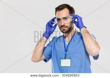 Portrait of serious young medical specialist working in hospital and wearing disposable sterile gloves isolated over white background