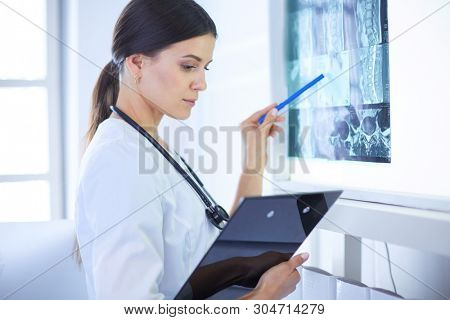 Young smiling female doctor with stethoscope pointing at X-ray at doctor's office