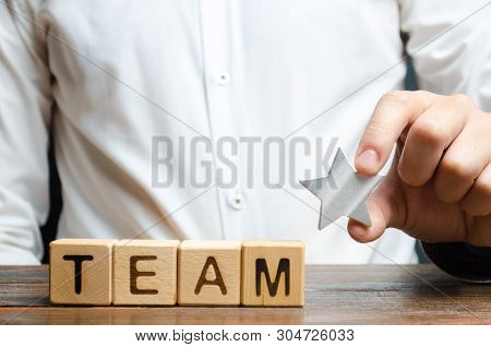 Businessman Hands A Star To The Team Near The Inscription Team On The Cubes. Concept Of Recognition 