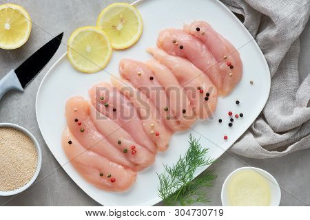 Raw Chicken Fillet. Meat With Breadcrumbs, Herbs , Lemon And Cooking Oil. Top View On Light Stone Ba
