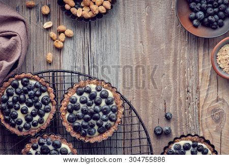 Top View On Wholegrain Blueberry Tarts With Vanilla Cream On Rustic Wooden Background