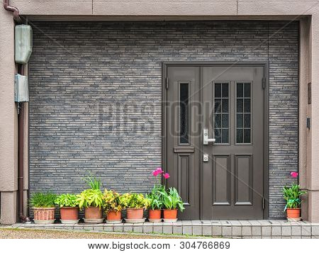 Gray Front Door With Small Square Decorative Windows And Flower Pots In Fron Of It