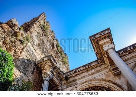 The Plane Leaving A Condensation Trail Flies High Above The Gates Of Hadrian. Adrian Gate, Antalya L