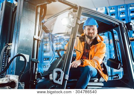 Proud worker in warehouse sitting in his forklift 