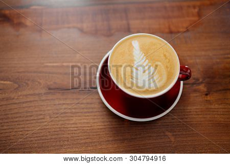 A Cup Of Cappucino In A Red Cup On A Sunny Morning, Waiting On A Wooden Table To Be Tasted.