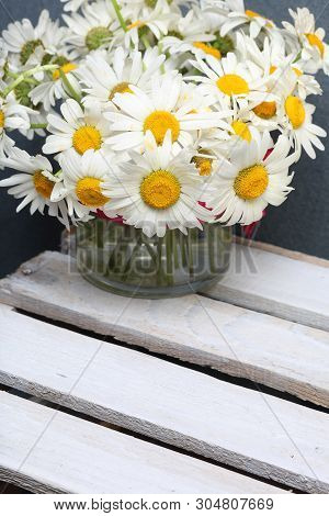 A Bouquet Of Field Daisies In A Glass Vase. On The  Wooden Boards. Genus Of Perennial Flowering Plan