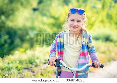 Smiling girl riding small modern bike with colorful jacket outdoors