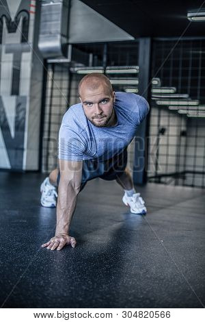 Portrait Of A Handsome Man Doing Push Ups Exercise With One Hand In Fitness Gym. Dressed In A Sports