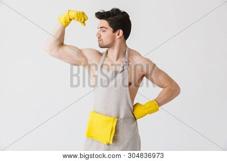 Handsome shirtless brunette houseman wearing apron standing isolated over white background, flexing muscles
