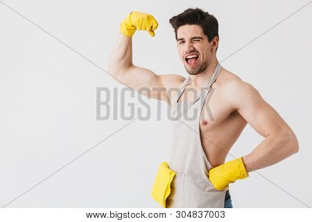 Handsome shirtless brunette houseman wearing apron standing isolated over white background, flexing muscles