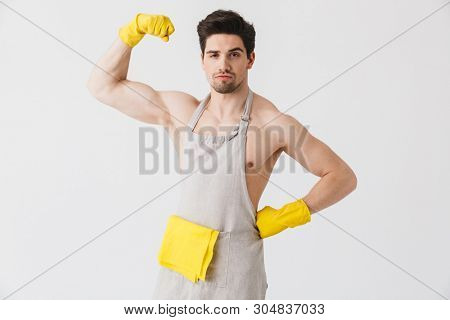 Handsome shirtless brunette houseman wearing apron standing isolated over white background, flexing muscles
