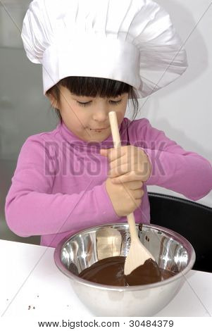 Bambina cucina cioccolato in cucina.Bambina usando un tappo di chef e la cottura in una cucina.