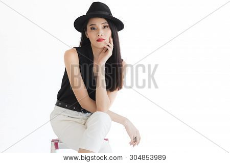Sexy Asian Model Woman In Black Shirt And White Pants, Wearing Hat, Standing And Pompous, Studio Sho