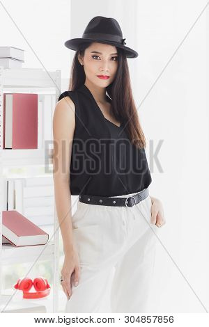 Sexy Asian Model Woman In Black Shirt And White Pants, Wearing Hat, Standing And Pompous, Studio Sho