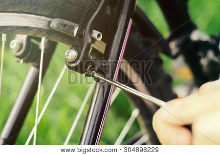 A Man Unscrews The Bolts With A Screwdriver On The Mount Wheel Brakes Of A Mountain Bike On The Back