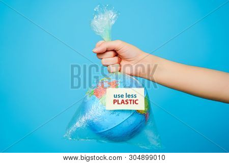 Woman holds in hands plastic bag and planet earth with text sticker- Use LESS PLASTIC at blue background. The concept of plastic pollution.