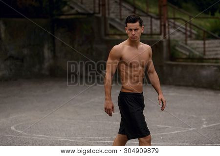 Handsome Shirtless Young Sportive Man, Sitting On Bascketball Court, Showing His Six Pack Abs, Toned