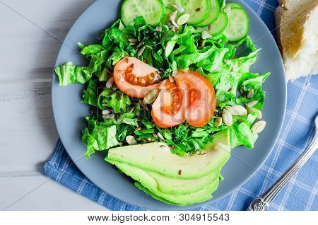 Fresh  Green Salad With Cucumber, Lettuce, Avocado And Tomatoes And Glass Water On A White Wooden Ta